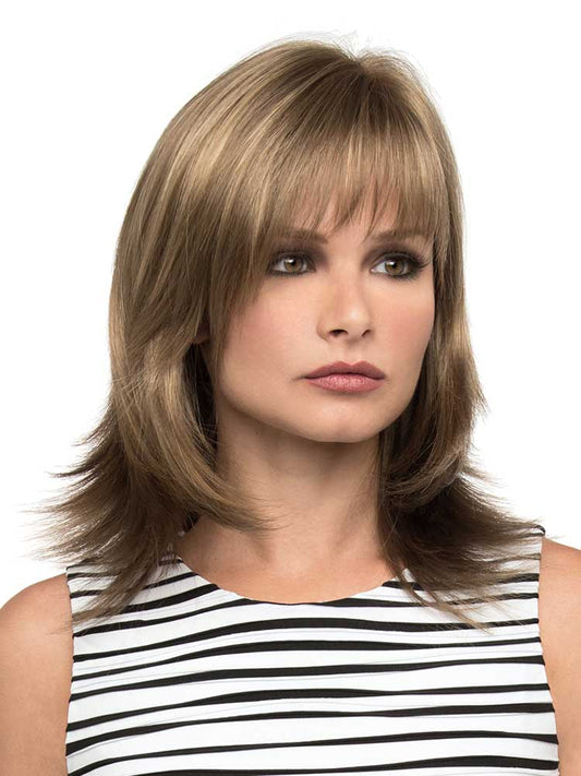 A woman wearing a shoulder-length wig with long, gentle layers and a wispy, face-framing fringe in an almond breeze color.